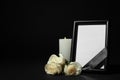 Funeral photo frame with ribbon, white roses and candle on dark table against black background Royalty Free Stock Photo