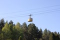 The funicular of yellow color slides on wires over tops of green trees against the background of the blue sky