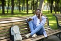 Funky African American guy sitting on bench and enjoying music on mobile phone at park, free space Royalty Free Stock Photo