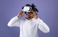 Funky Afro teen wearing VR headset, exploring cyberspace, using virtual reality for entertainment on violet background Royalty Free Stock Photo