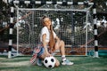 Funky young blonde teenage hipster girl posing with serious face with soccer ball in front of goal post at the stadium Royalty Free Stock Photo