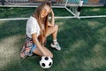 Funky young blonde teenage hipster girl posing with serious face with soccer ball in front of goal post at the stadium Royalty Free Stock Photo