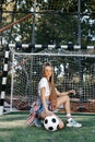 Funky young blonde teenage hipster girl posing with serious face with soccer ball in front of goal post at the stadium Royalty Free Stock Photo