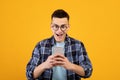 Funky young man using cellphone for online communication, work or learning on orange studio background Royalty Free Stock Photo