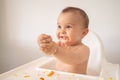 A funny adorable and dirty little baby girl of 6 months eats while sitting in the baby chair Royalty Free Stock Photo