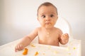 Funny adorable and dirty little baby girl of 6 months eats while sitting in the baby chair Royalty Free Stock Photo