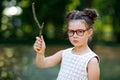 Funny adorable little kid girl with glasses and wooden magic wand playing Harry Potter in park on sunny day. Royalty Free Stock Photo