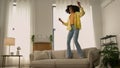 Funny African American woman happy girl at home dancing jumping have fun fooling joy testing comfortable soft couch cozy Royalty Free Stock Photo