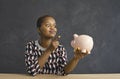 Funny african american woman punishing waving her finger to the piggy bank in her hand.