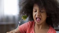 Funny African girl eating broccoli with huge disgust, healthy diet for children