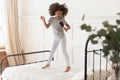 Funny african kid girl jumping on bed singing in hairbrush Royalty Free Stock Photo