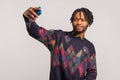Funny african man with dreadlocks and beard holding smartphone in hand and posing at camera making selfie, camera application Royalty Free Stock Photo