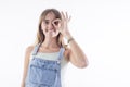 Funny amusing blonde girl in jeans dress showing okay gesture near her eye