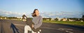 Funny asian girl enjoying skating, holding skateboard like guitar and shadow playing, having fun outdoors