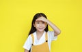 Funny asian little child girl shielding her eyes by hand on forehead on yellow background. Child expression searching