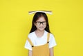 Funny asian little child girl wearing glasses with book on head and looking camera isolated on yellow background. Student and Royalty Free Stock Photo