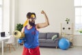 Funny athlete holding gym mat and dumbbells and showing his weak biceps after sport workout at home Royalty Free Stock Photo
