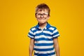 Funny attractive boy wearing glasses and blue striped polo, making grimace against yellow background Royalty Free Stock Photo