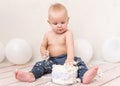 Funny baby boy eating cake witn balloons on the background. Dirty kid face and hands in the cream. first birthday celebration