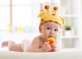 Funny baby boy in giraffe hat lying on his belly in nursery. Little kid using nibbler toy. Royalty Free Stock Photo