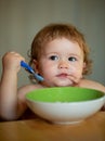 Funny baby eating food himself with a spoon on kitchen. Healthy nutrition for kids. Royalty Free Stock Photo