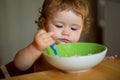 Funny baby eating food himself with a spoon on kitchen. Healthy nutrition for kids. Royalty Free Stock Photo