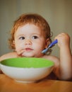 Funny baby eating food himself with a spoon on kitchen. Healthy nutrition for kids. Royalty Free Stock Photo