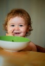 Funny baby eating food himself with a spoon on kitchen. Smiling baby eating food. Funny child face closeup. Launching Royalty Free Stock Photo