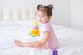 funny baby girl in pink bodysuit playing with plastic toy children pyramid on bed