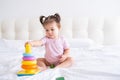 funny baby girl in pink bodysuit playing with plastic toy children pyramid on bed