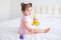 funny baby girl in pink bodysuit playing with plastic toy children pyramid on bed