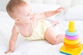 funny baby girl in yellow bodysuit playing with plastic toy children pyramid on bed