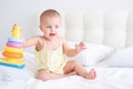 funny baby girl in yellow bodysuit playing with plastic toy children pyramid on bed