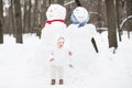 Funny baby next to a snowman in a winter park
