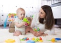 Funny baby and young woman playing in nursery. Happy family having fun with colorful toys at home.