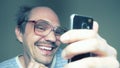 Funny balding man in glasses uses a smartphone and smiles