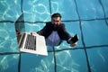 Funny bearded business man in suit using phone and laptop in swimming pool. Concept of young people working mobile Royalty Free Stock Photo