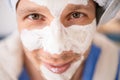 Young man with a cosmetic mask on his face in bathrobe and a towel on his head makes spa treatments on his face resting at