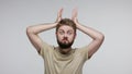 Funny bearded man doing antler gesture, bull horns on his head and looking at camera with menace expression