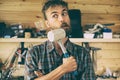 Funny bearded worker man stands in workshop and hits himself with a mallet, construction carpentry tools in the background. Funky