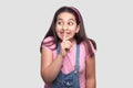 Funny beautiful brunette young girl in casual pink t-shirt, blue overalls standing, telling secret, toothy smile and looking away Royalty Free Stock Photo