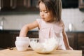 Funny beautiful little girl is taking salt from the salt cellar with fingers to add to the dough