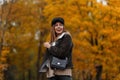 Funny beautiful young woman in a brown stylish jacket in an elegant hat with a visor with a leather fashion bag posing in the park Royalty Free Stock Photo