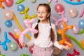 Funny birthday kid. Playing time. little girl with braids standing against gray wall decorated with colorful balloons, smiling Royalty Free Stock Photo