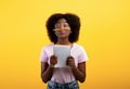 Funny black female student keeping pencil between nose and lips as moustach and holding notebook, yellow background Royalty Free Stock Photo