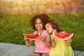 Funny Black girl and European girl are eating watermelon outdoors in the hot summer. Smiling children, healthy food Royalty Free Stock Photo