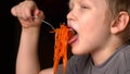 Funny blond boy is eating Korean carrot salad in kitchen next to his brother. Children are happy together