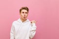 Funny blond guy in white casual clothes looks away with shocked face and points his finger at copy space. Portrait of surprised Royalty Free Stock Photo