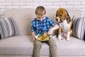 Funny boy with dog beagle eating fried potatoes with a hamburger