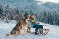 Funny boy with dog having fun with a sleigh in winter. Children with wolves dog. Winter vacation concept. Pet love. Royalty Free Stock Photo